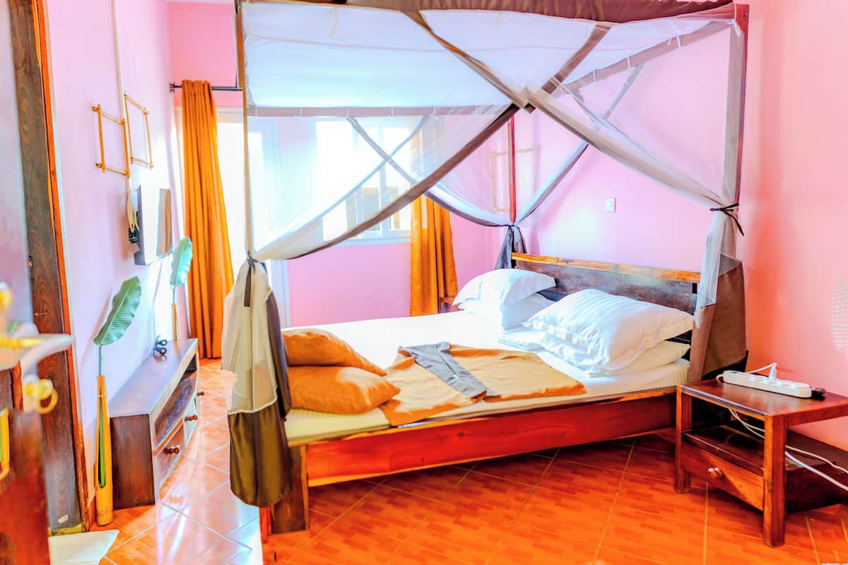 A bedroom with a wooden bed, a mosquito net, and a bedside table.