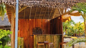Una zona de bar con barra de madera, taburetes, pared de bambú y techo de paja.