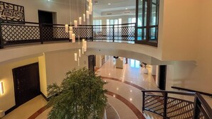 En rymlig hotellobby med högt i tak, modern takbelysning, en central trappa och ett stort fönster som släpper in naturligt ljus.
