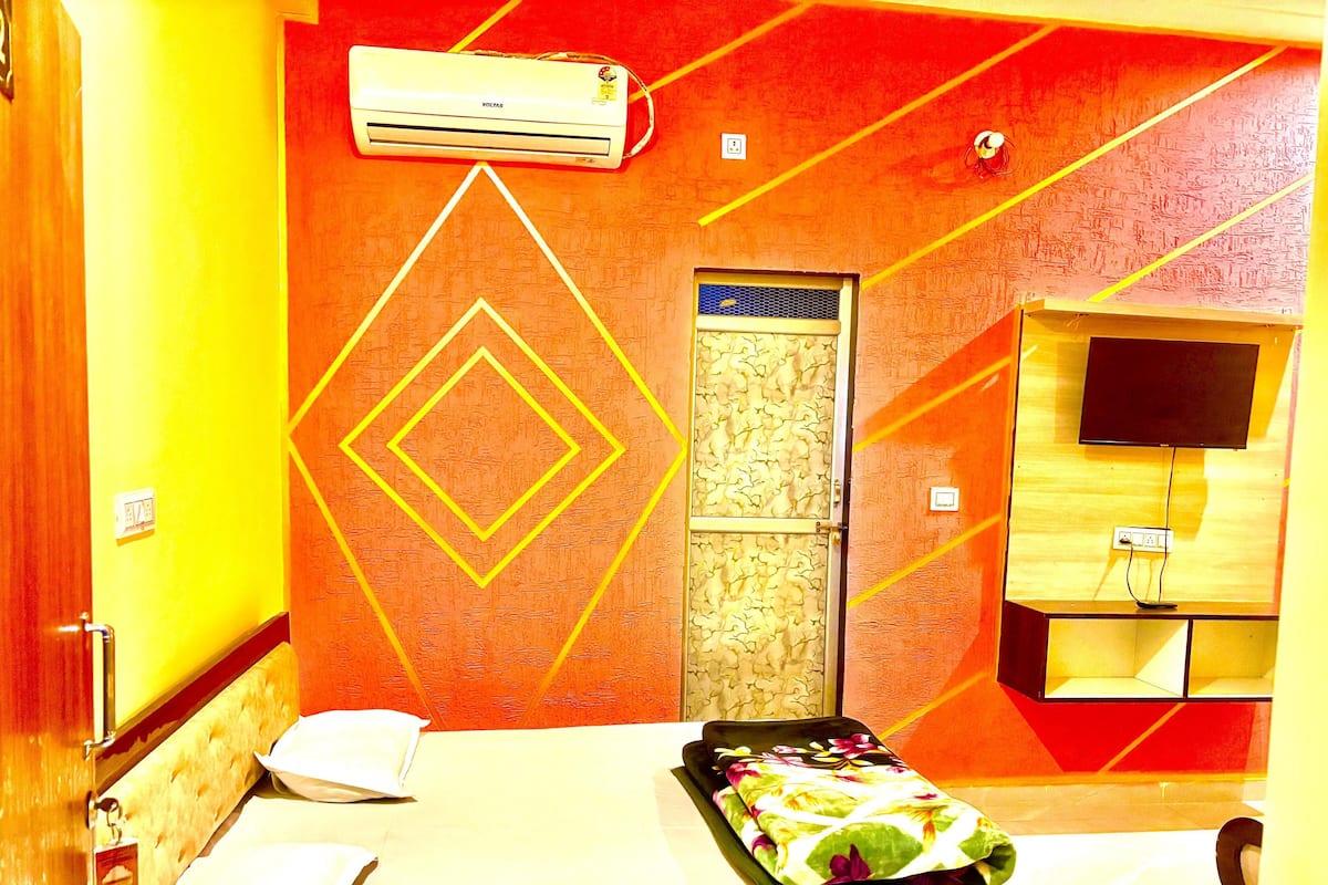 A hotel room with a bed, a TV, an air conditioner, and a patterned wall.