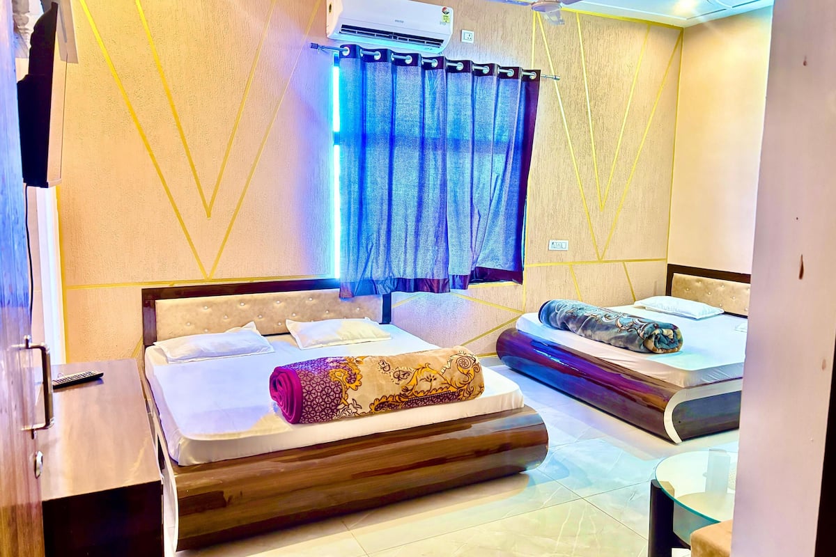 A hotel room with two beds, a ceiling fan, an air conditioning unit, and a small table with a glass top.