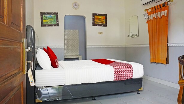A neatly made bed with white and red bedding, a wooden door, a wall-mounted air conditioner, and two framed pictures. - OYO 90369 Syariah An Nur (Cigombong)
