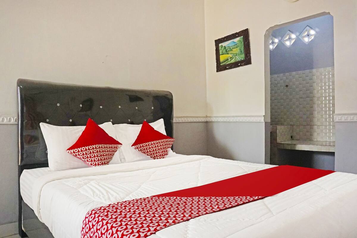 Un lit bien fait, avec une literie blanche rehaussée de touches de rouge, une tête de lit et un plaid rouge.