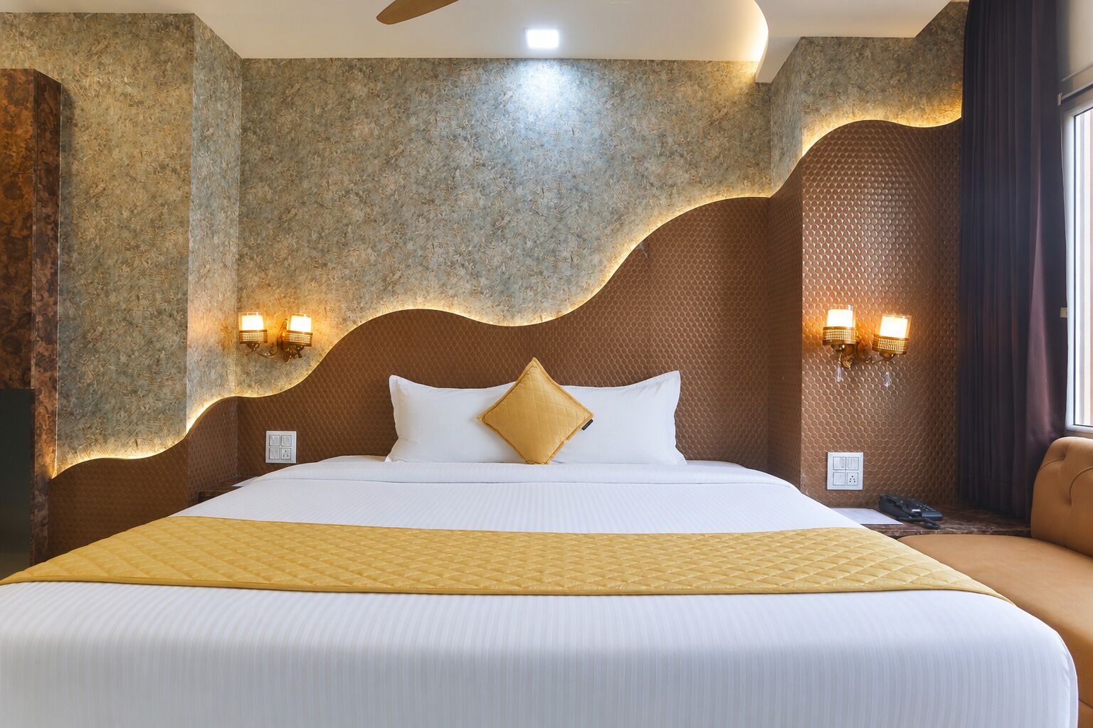 Une chambre d’hôtel avec un grand lit, deux lampes fixées au mur et un décor mural texturé.