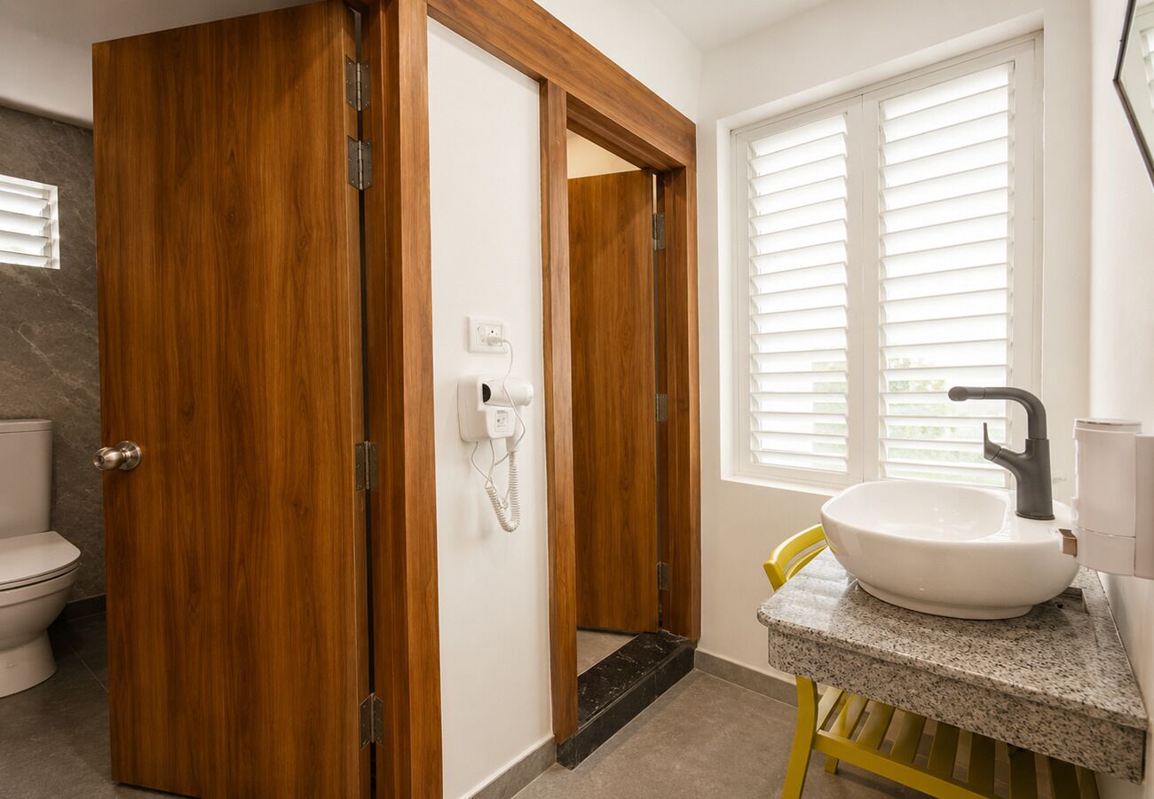 A bathroom with a wooden door, a white sink, a yellow chair, and a toilet.