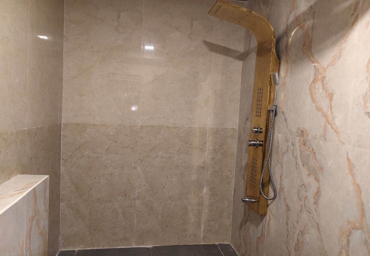 A bathroom with a shower, marble walls, and a wooden showerhead.