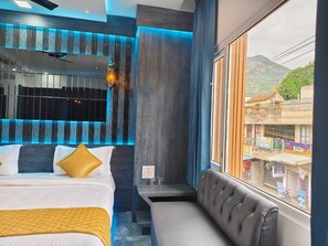 Habitación de hotel moderna con cama, zona de estar, vistas al exterior y una pared con líneas verticales.