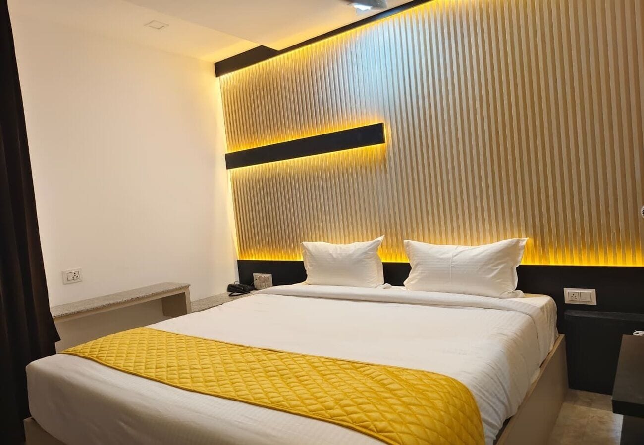 Una habitación de hotel con una cama grande, un cabecero con líneas verticales y un detalle amarillo en la colcha.