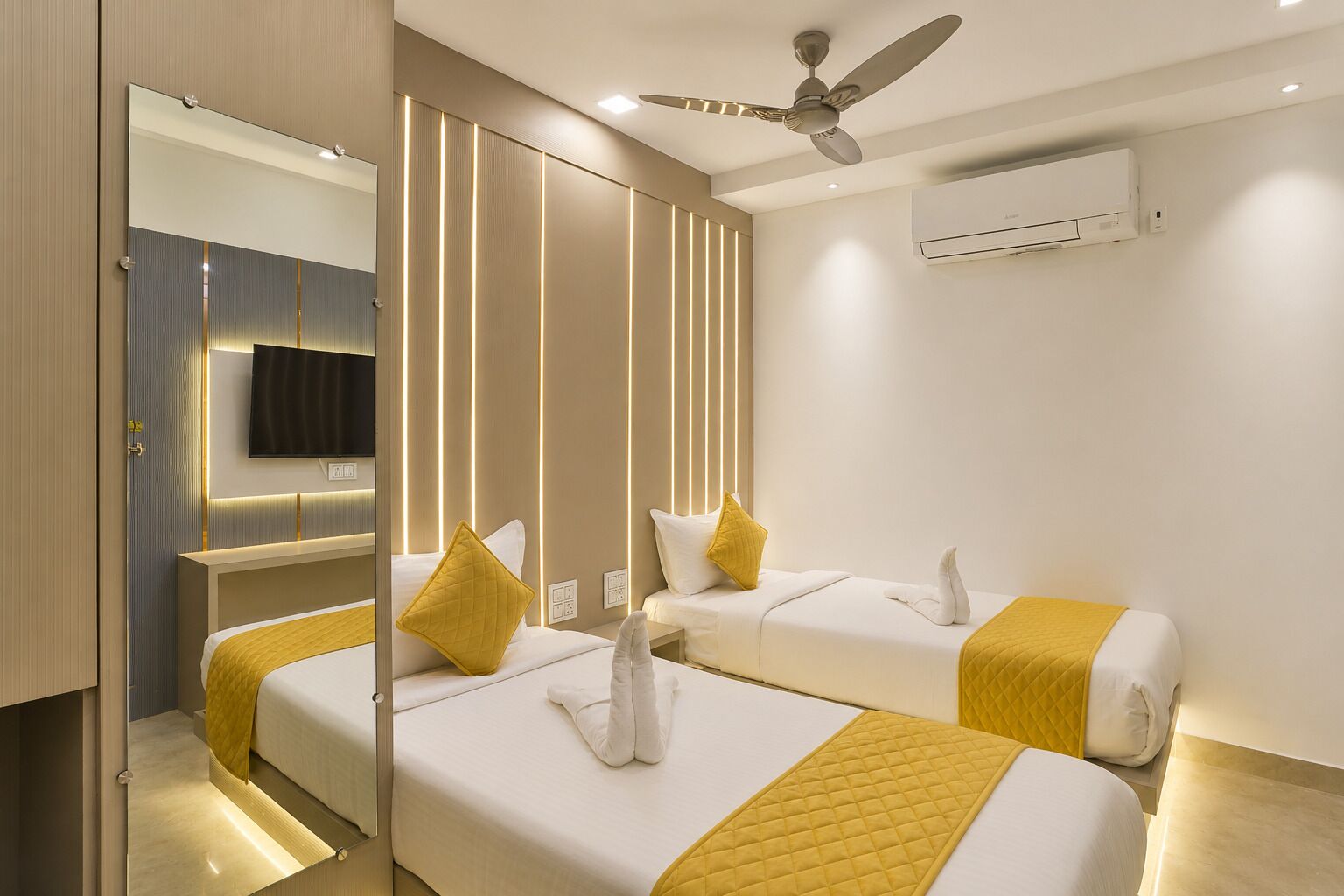 A hotel room with two beds, a ceiling fan, an air conditioning unit, and a television.