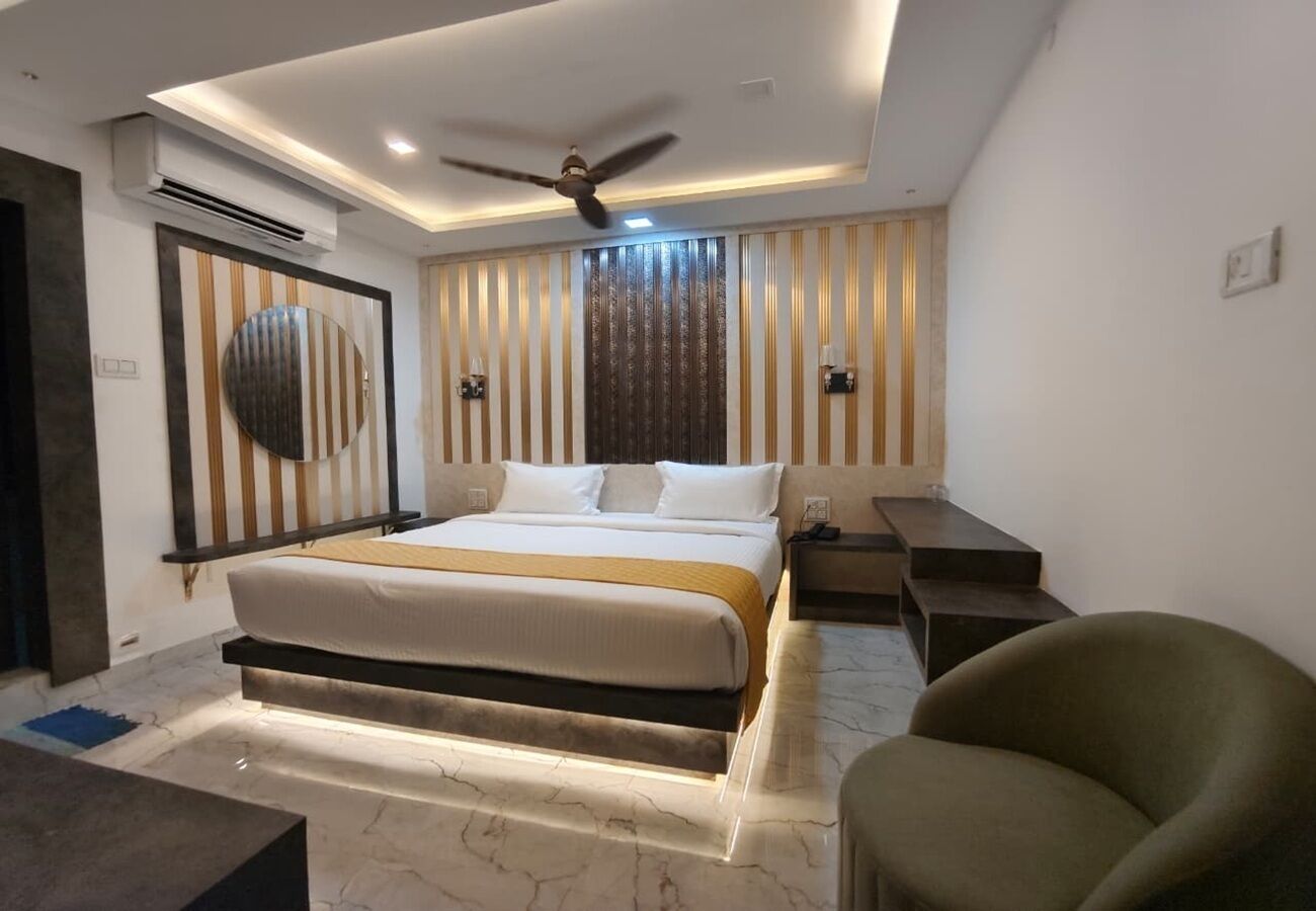A modern hotel room with a large bed, a ceiling fan, an air conditioning unit, a desk, and a chair.