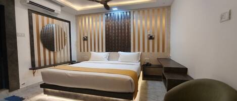 A modern hotel room with a large bed, a ceiling fan, an air conditioning unit, a desk, and a chair.