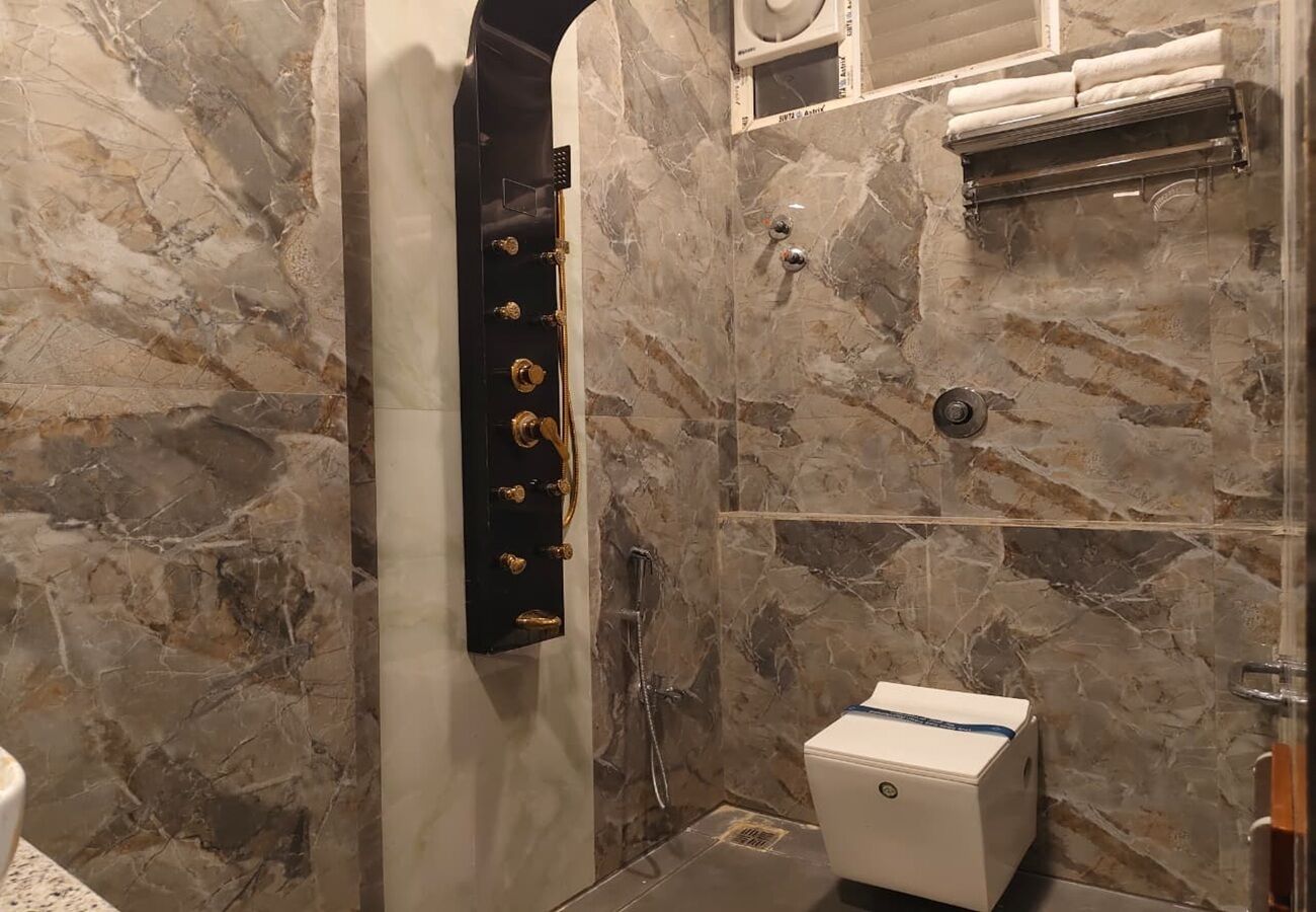 Une salle de bain avec un mur en marbre, un porte-serviettes noir, une douche et des toilettes.