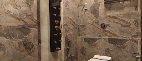 Une salle de bain avec un mur en marbre, un porte-serviettes noir, une douche et des toilettes.
