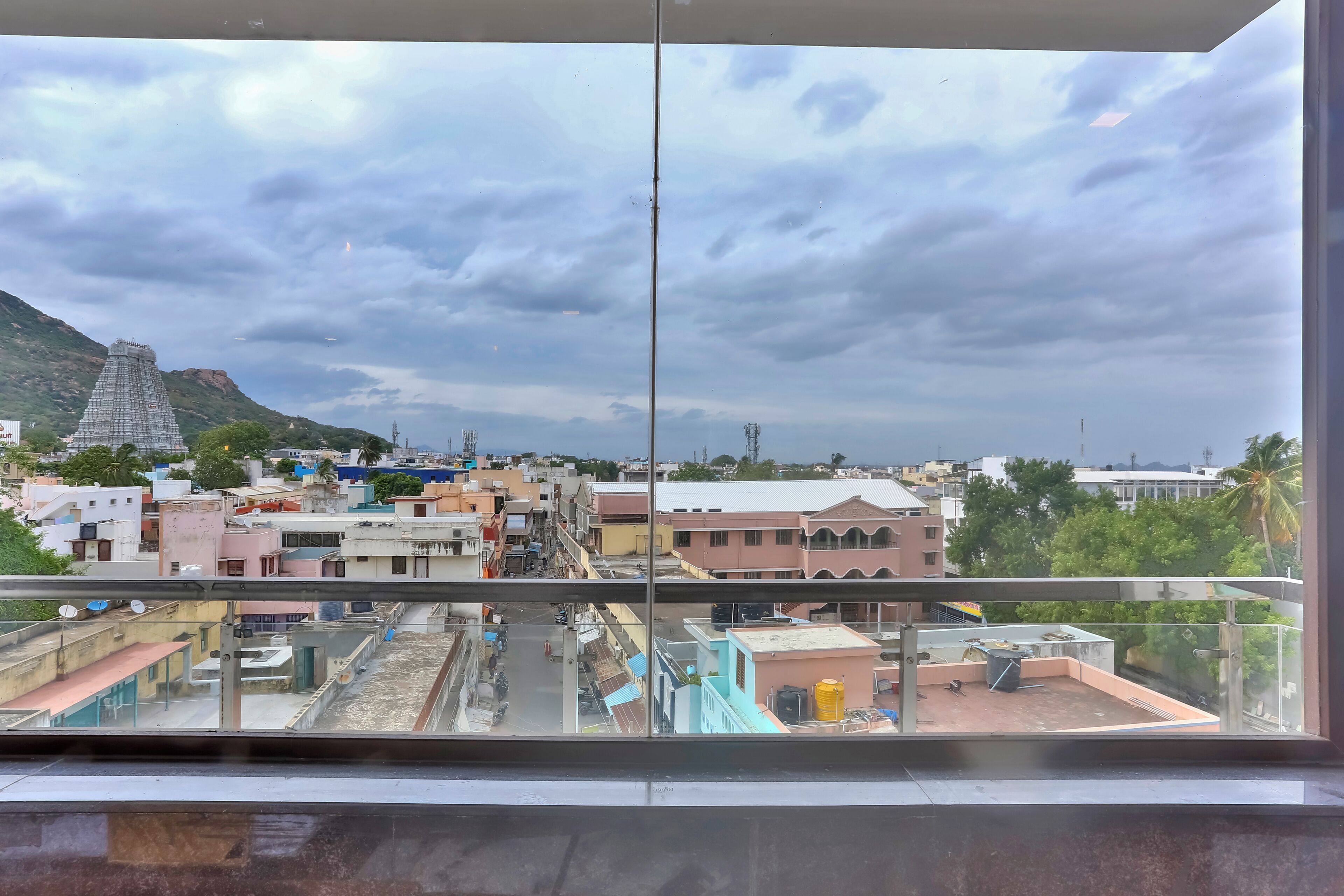 Une vue depuis une fenêtre donnant sur un paysage urbain, avec des bâtiments, une colline et un ciel dégagé.