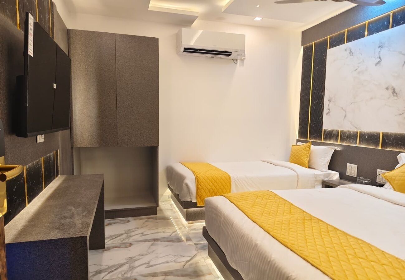 A hotel room with two beds, a desk, a wardrobe, and an air conditioning unit.
