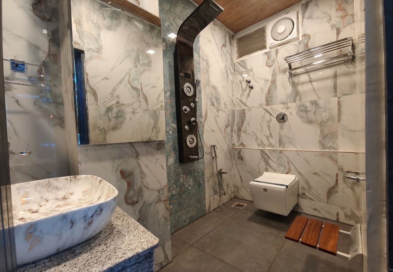 Een badkamer met een marmeren wastafel, een douche met regendouche, een toilet en een houten bankje.