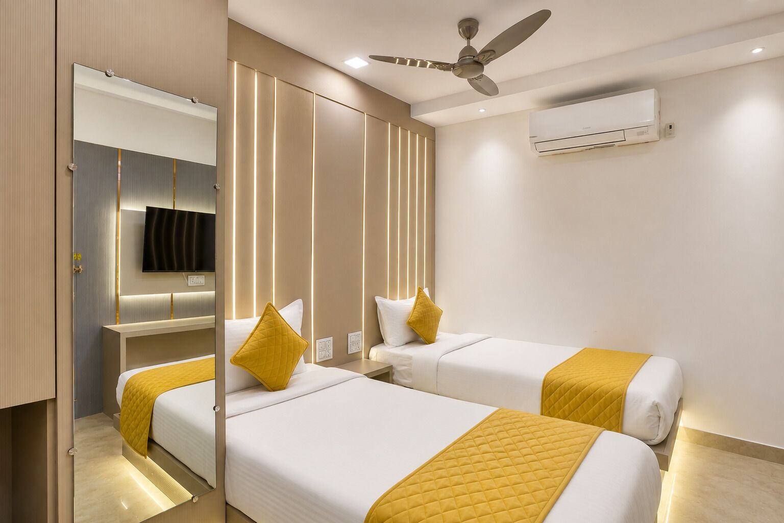 A hotel room with two beds, a ceiling fan, an air conditioning unit, and a television on the wall.
