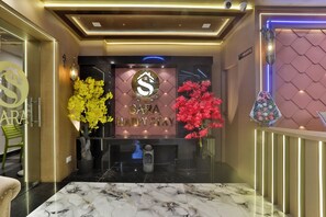 Zona de recepción con piso de mármol, mostrador de recepción y plantas decorativas.