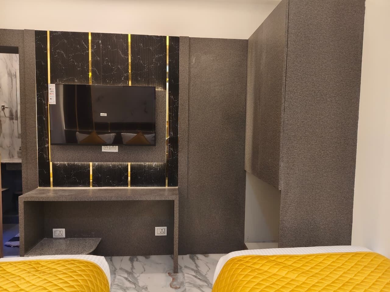 Ein Zimmer mit zwei Betten, einem integrierten Fernseher und einer Wand mit Grau-Struktur.