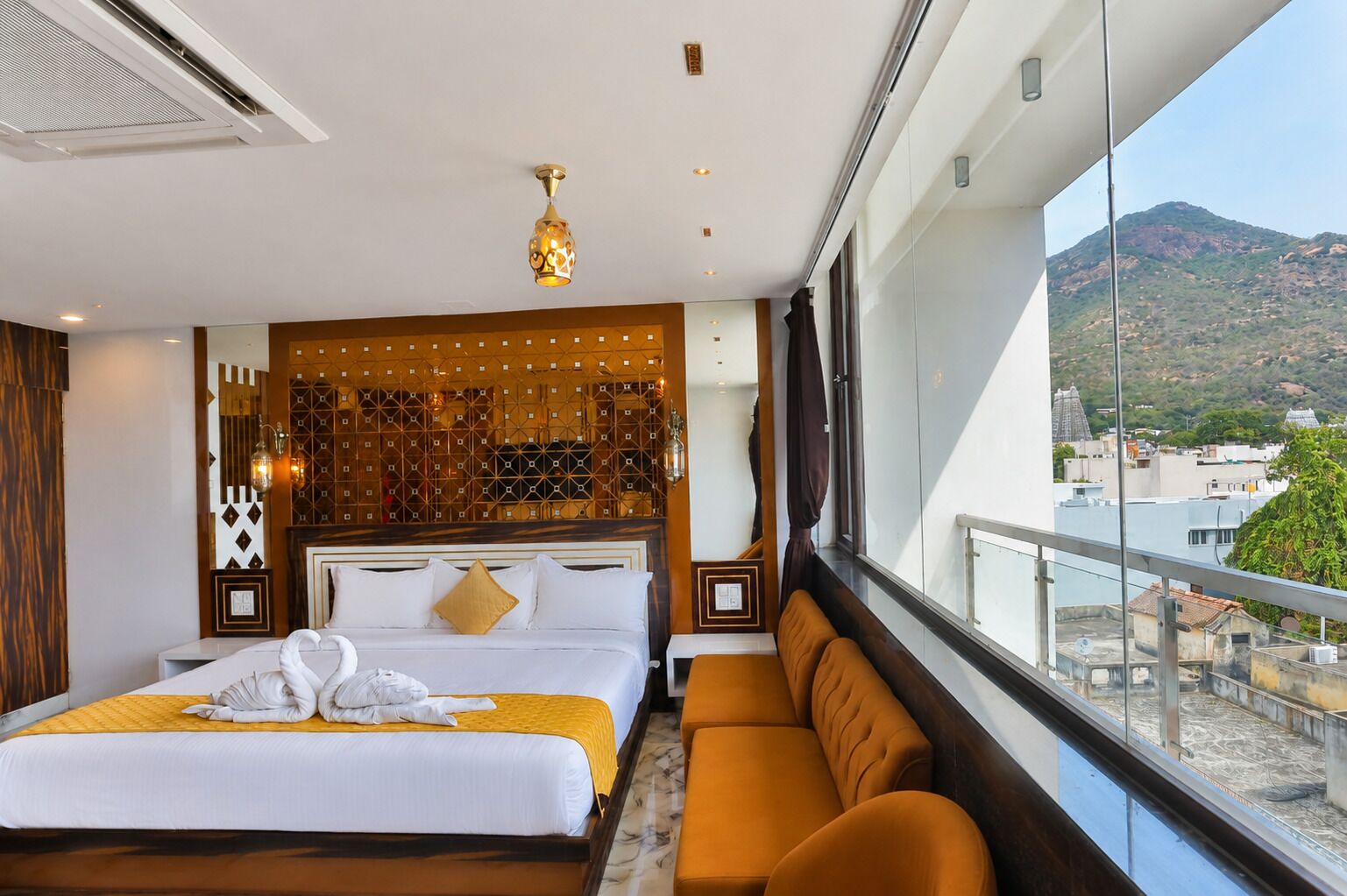 A hotel room with a large bed, a sofa, a decorative wall, and a view of the city.