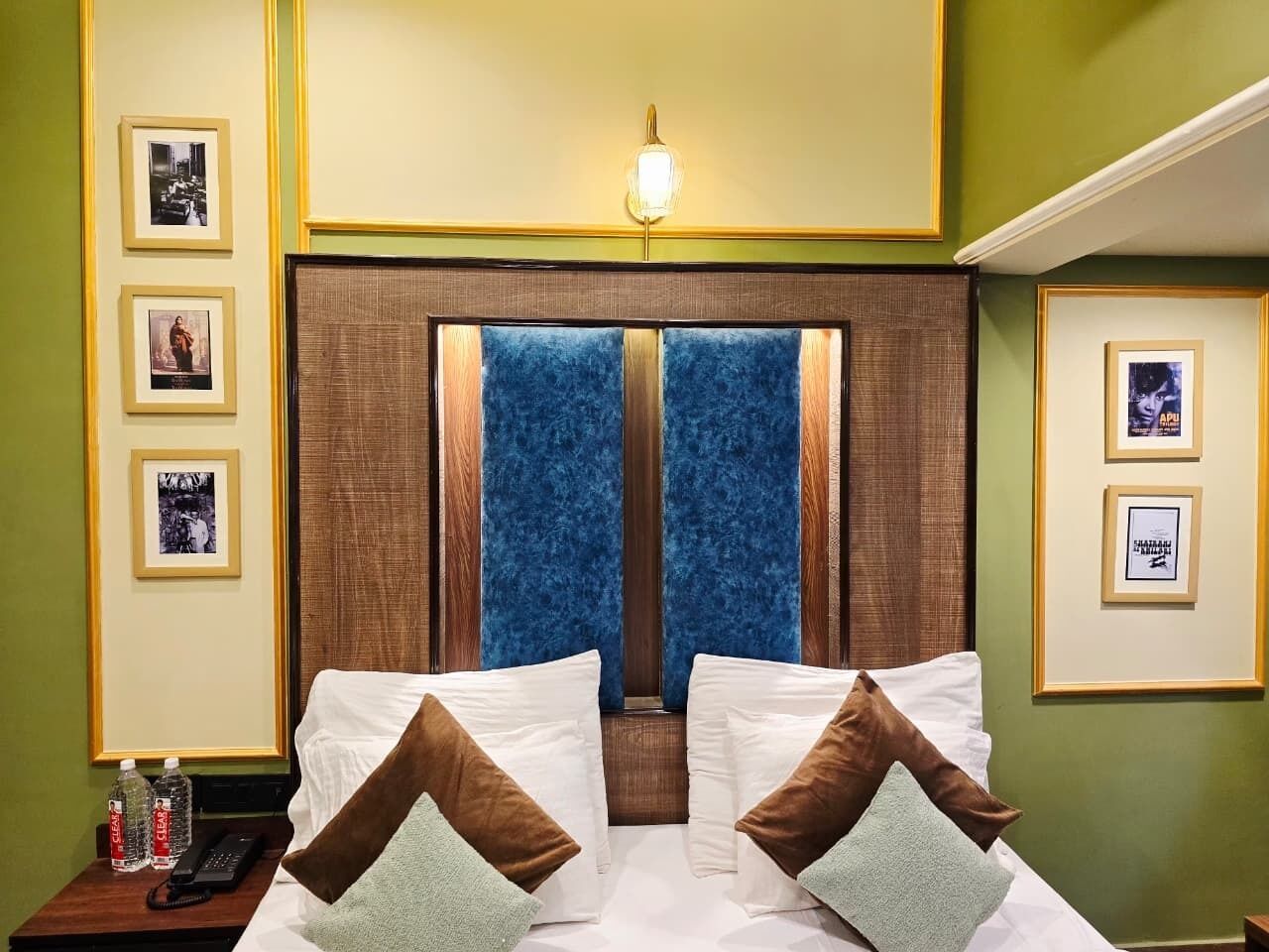 A hotel room with a large bed, two pillows, a nightstand with a phone, and framed pictures on the walls.