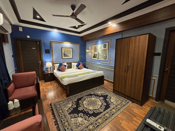 A bedroom with a bed, a chair, a wardrobe, and a ceiling fan. - Hotel Trimoorti (Kolkata)