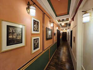 A hallway with framed pictures on the walls, a wooden floor, and a green and white color scheme. - Hotel Trimoorti (Kolkata)