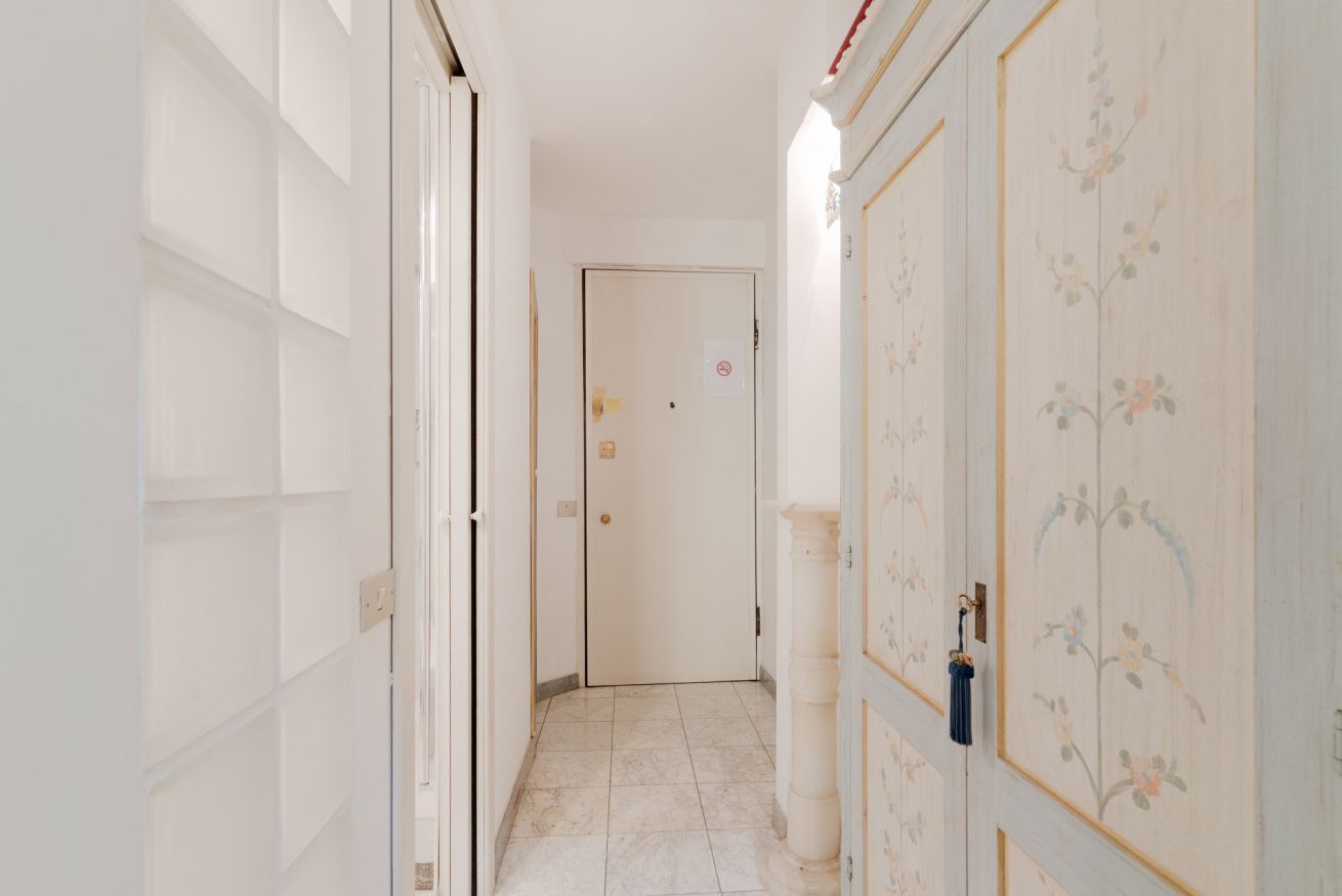 Un couloir étroit aux murs blancs, doté d’un sol carrelé et d’une porte au fond.