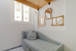 A small room with a single bed, a window with stained glass, and three wall-mounted mirrors.