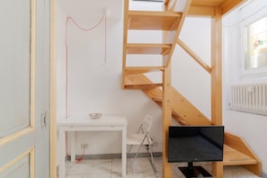 A room with a white desk, a chair, a wooden staircase, and a black TV stand.