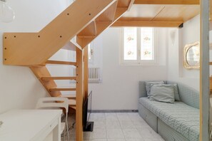 A compact room with a wooden staircase, a white desk, a green sofa, and a window with a radiator.
