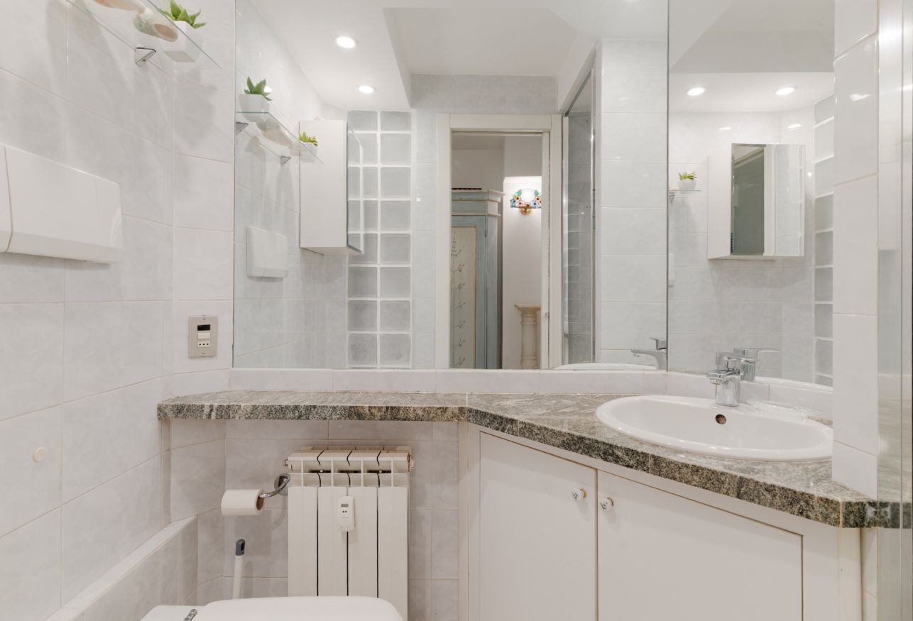 A modern bathroom with a white sink, a glass shower enclosure, and a marble countertop.
