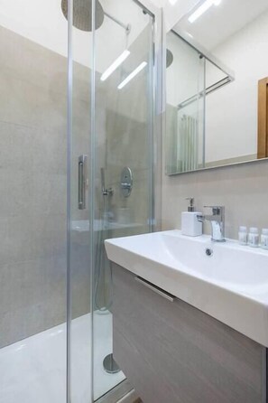 A modern bathroom with a glass-enclosed shower, a large vanity with a mirror, and a white sink. - Pallottole Duomo Apartments (Florence)
