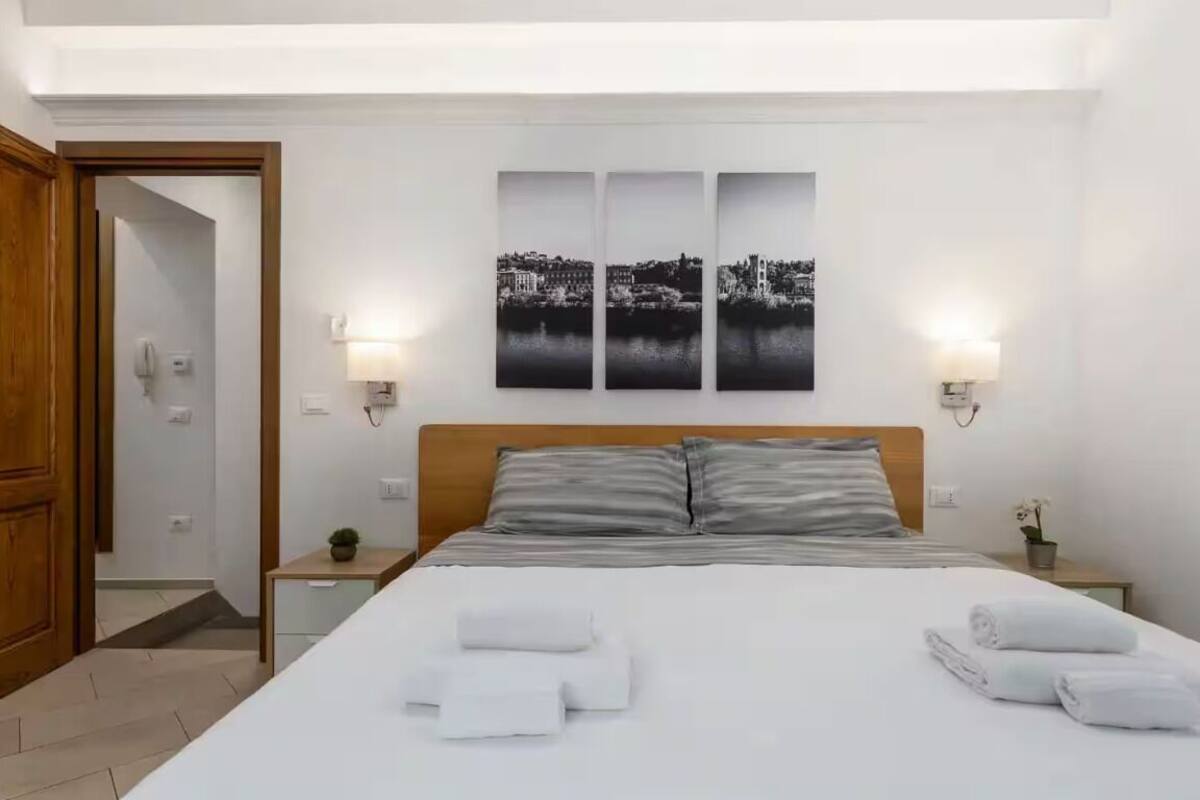 Habitación de hotel con una cama grande, dos mesitas de noche, un cabecero de madera y tres pinturas en blanco y negro con vistas urbanas en la pared.