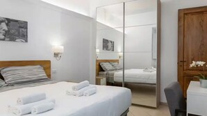 A hotel room with a bed, a desk, a chair, a wardrobe, and a mirror. - Pallottole Duomo Apartments (Florence)