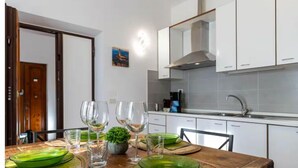 A modern kitchen with white cabinets, a stainless steel sink, and a dining area with a wooden table set for a meal. - Pallottole Duomo Apartments (Florence)