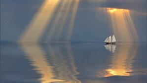 Um veleiro em águas calmas com raios de sol refletindo na superfície.