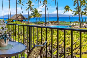 A balcony with a view of a swimming pool, palm trees, and the ocean.