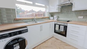 A compact kitchen with white cabinets, a dishwasher, an oven, and a window overlooking a residential area.