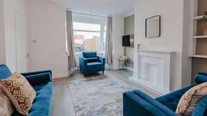 A living room with a blue sofa set, a patterned rug, a fireplace, and a television mounted on the wall.