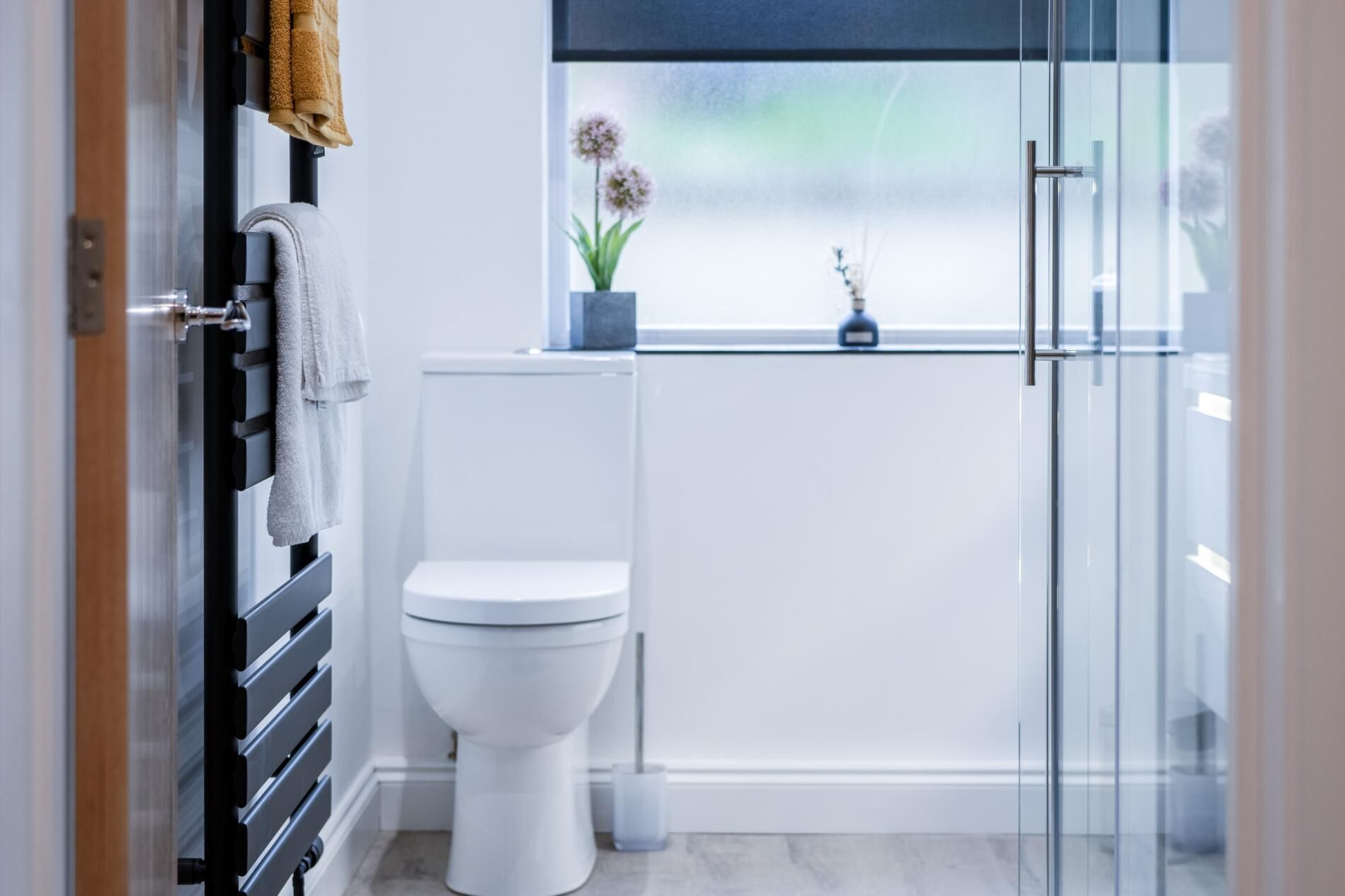 Un baño moderno con inodoro, cabina de ducha de vidrio y ventana con planta.