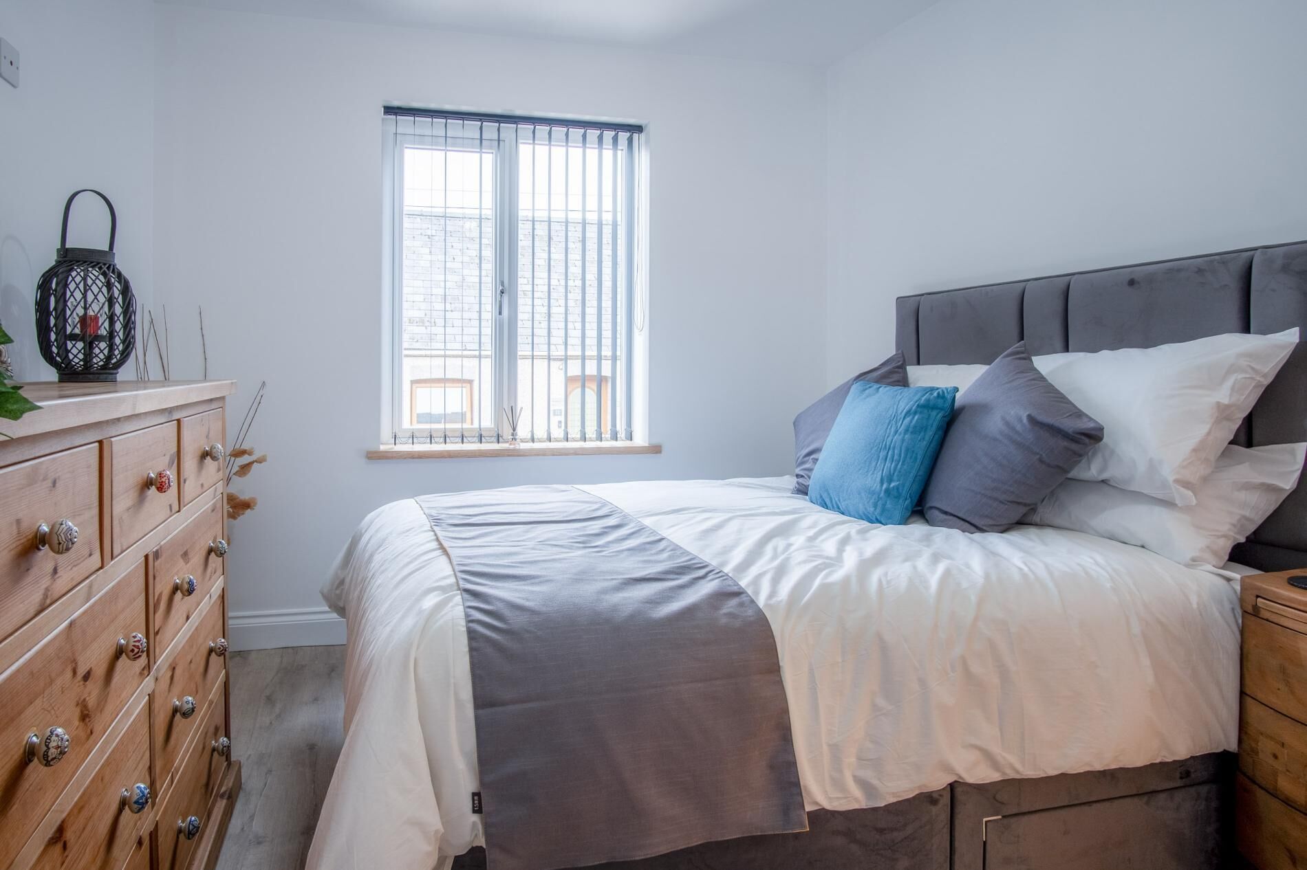 Un dormitorio con cama, cómoda de madera y ventana con persianas.