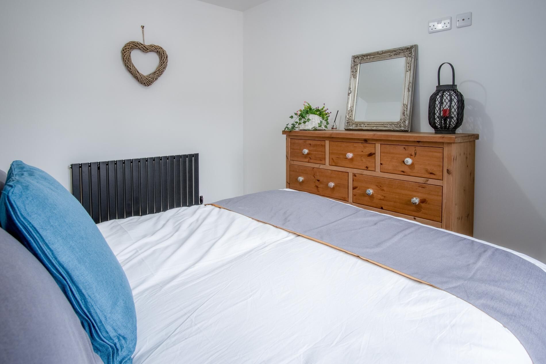 A bedroom with a bed, a dresser, a mirror, and a heart-shaped decoration on the wall.