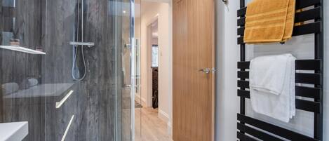 A modern bathroom with a glass-enclosed shower, a wooden door, and a towel rack with multiple towels.