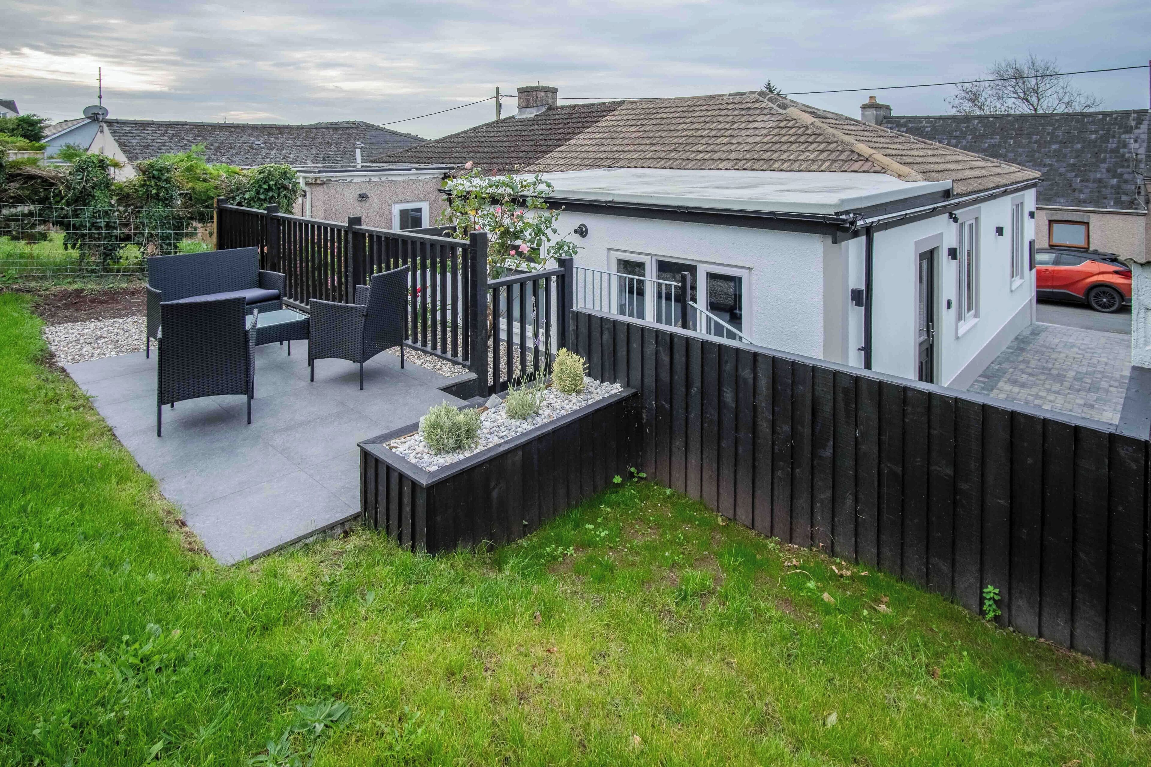 A modern house with a patio area featuring outdoor furniture and a garden bed.