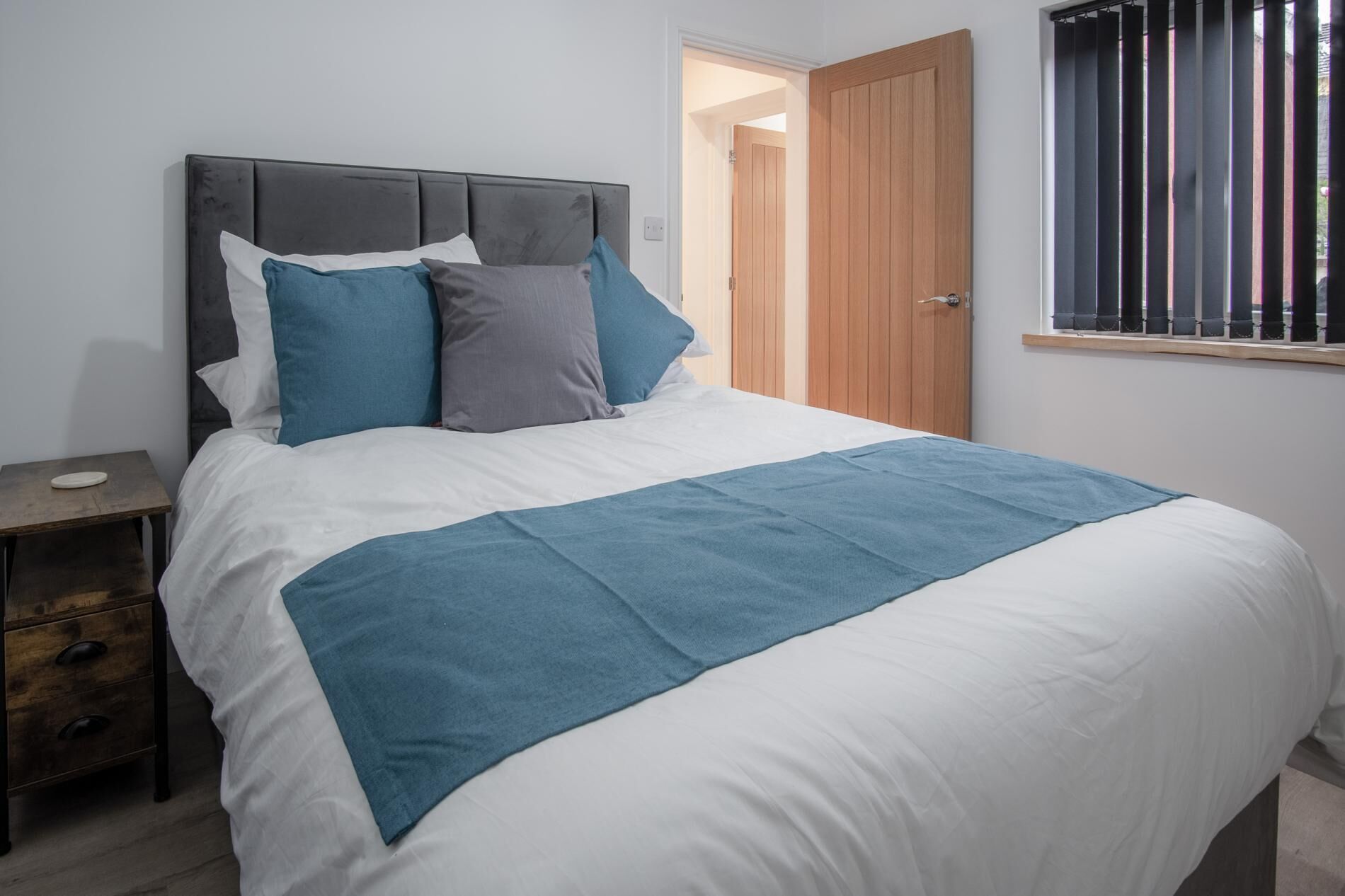 A neatly made bed with a white and blue bedspread, a dark headboard, and several pillows in shades of blue and gray.