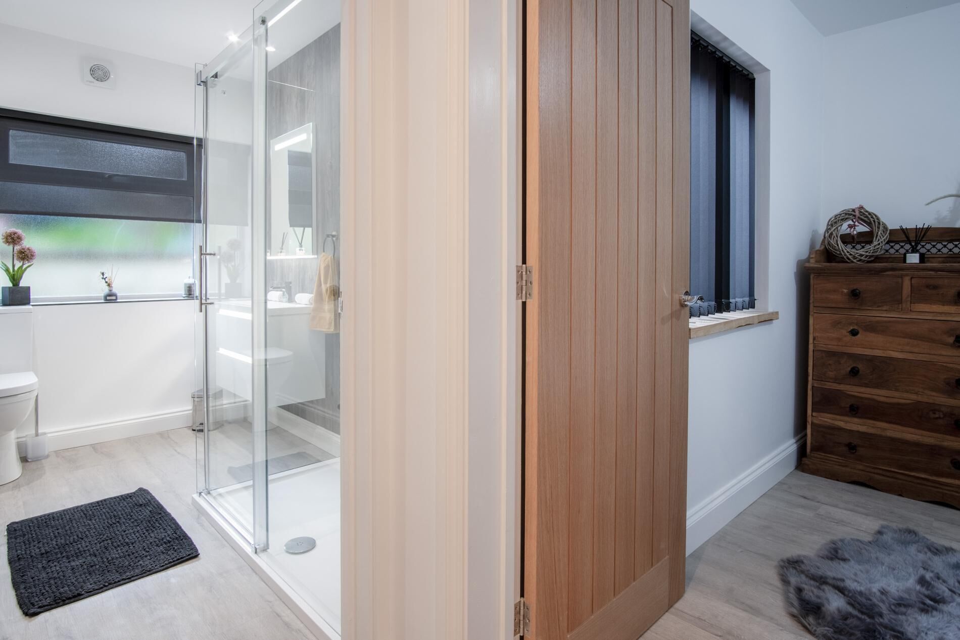 Un baño moderno con cabina de ducha de vidrio, un armario de madera y una ventana pequeña con cortinas.
