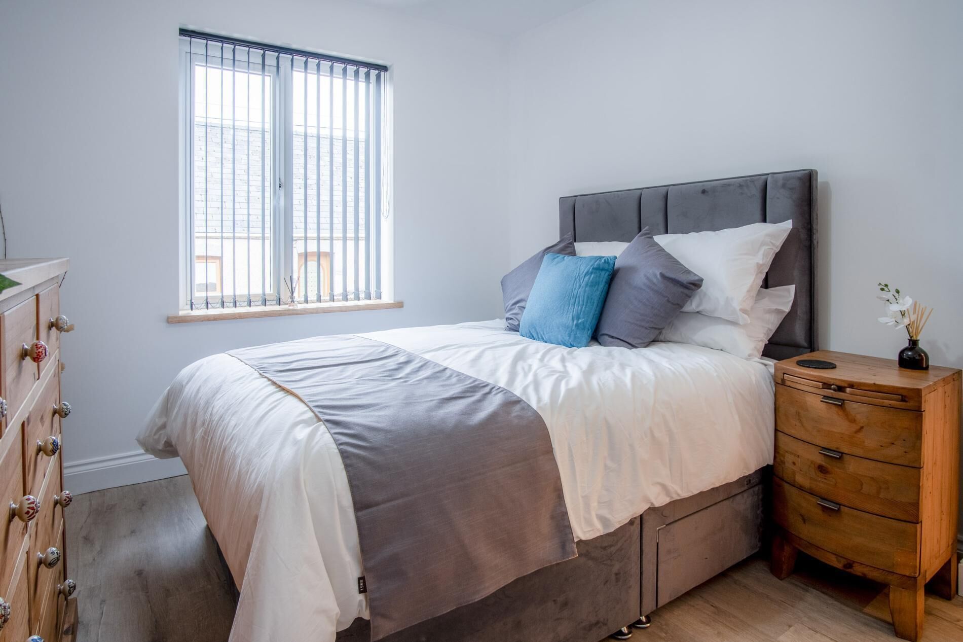 A bedroom with a bed, a nightstand, a dresser, and a window with blinds.