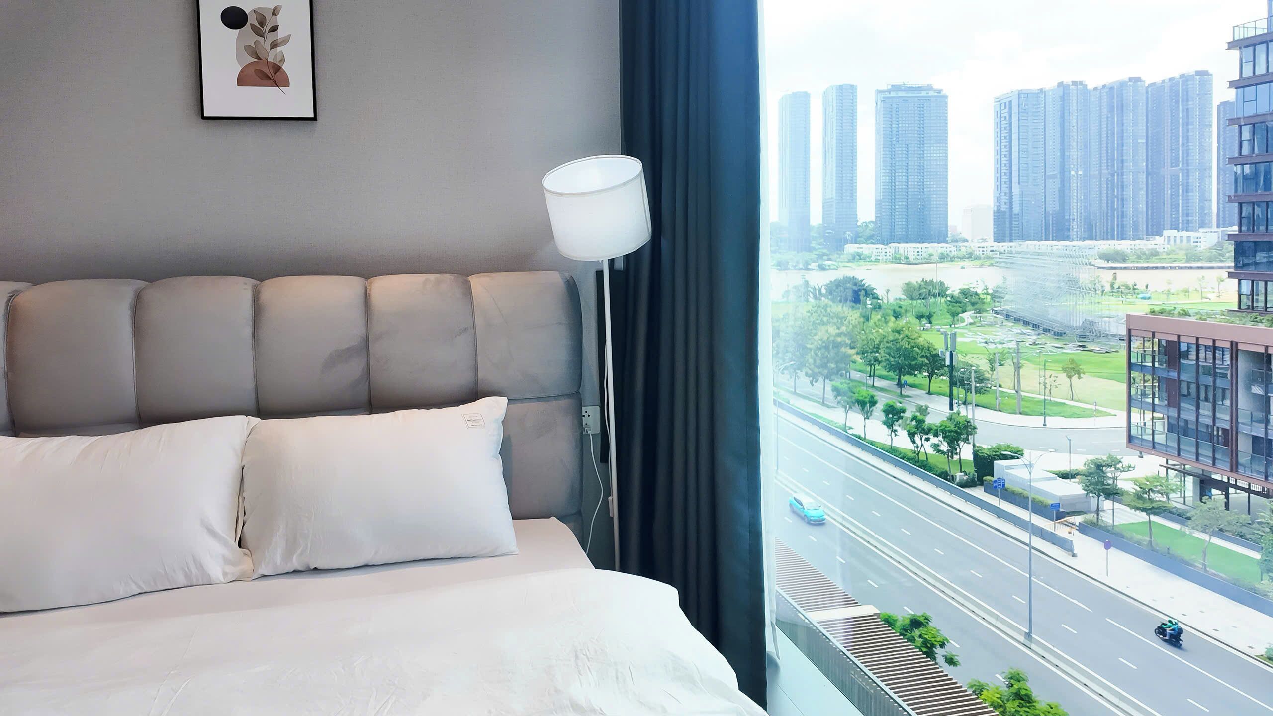 A modern hotel room with a large bed, a bedside lamp, and a city view.