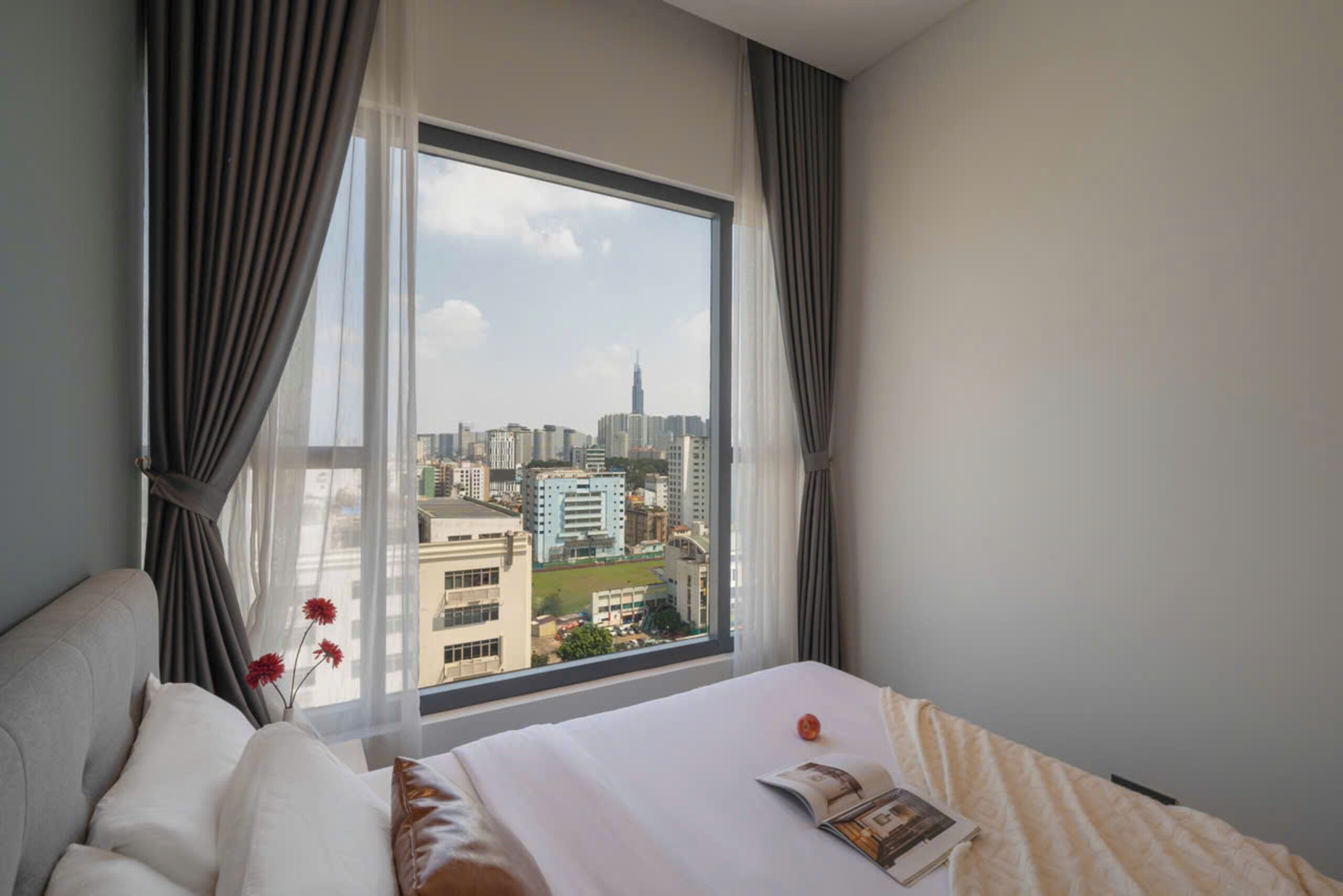 A hotel room with a large window, a bed, a chair, and a vase with flowers.